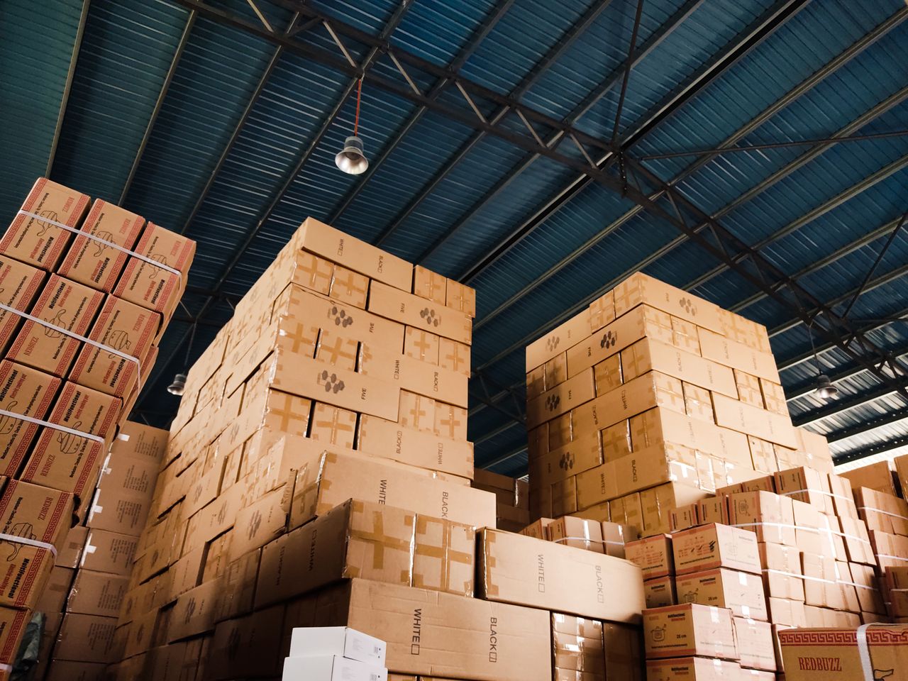 Home High stacks of cardboard boxes organized in a warehouse with a blue metal ceiling.